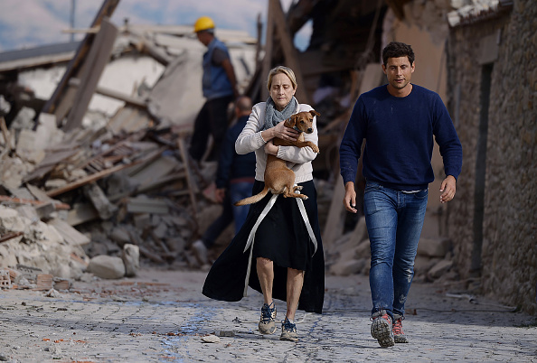 TOPSHOT - A woman holds a dog in her arms as she walks with a man next to the rubble of buildings in Amatrice on August 24, 2016 after a powerful earthquake rocked central Italy. The earthquake left 38 people dead and the total is likely to rise, the country's civil protection unit said in the first official death toll. Scores of buildings were reduced to dusty piles of masonry in communities close to the epicentre of the pre-dawn quake in a remote area straddling the regions of Umbria, Marche and Lazio. / AFP / FILIPPO MONTEFORTE (Photo credit should read FILIPPO MONTEFORTE/AFP/Getty Images)